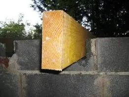 Poutre en bois reposant sur des blocs de béton, illustrant un chantier de construction en cours.