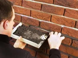 Homme appliquant du mortier sur un mur en briques, utilisant une truelle pour le pose soignée.